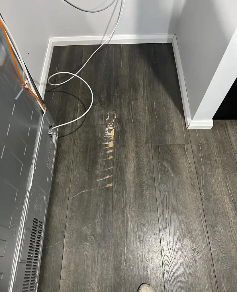Scratched laminate floor before repair near kitchen fridge
