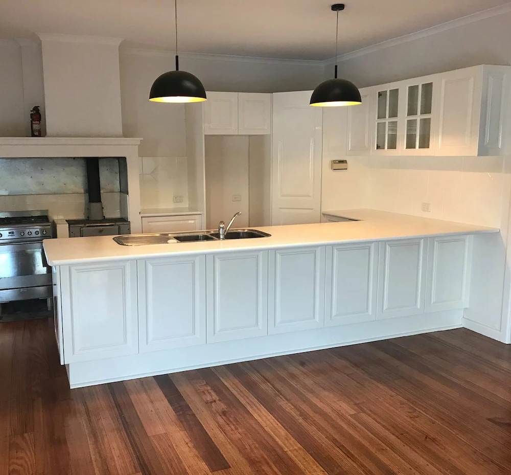 Modern white kitchen featuring a resurfaced benchtop and stainless steel appliances.