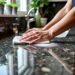 Person cleaning a granite benchtop with a cloth.