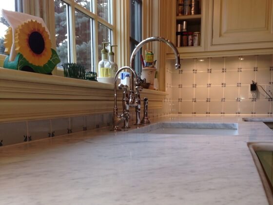 Dull and faded marble kitchen benchtop with a faucet and window in the background.