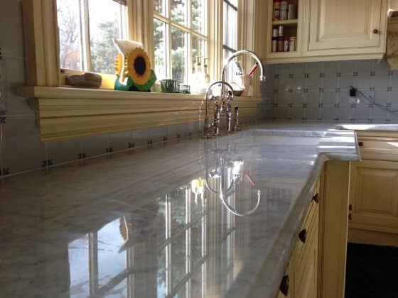 Polished and gleaming marble kitchen benchtop reflecting light, with a faucet and window in the background.
