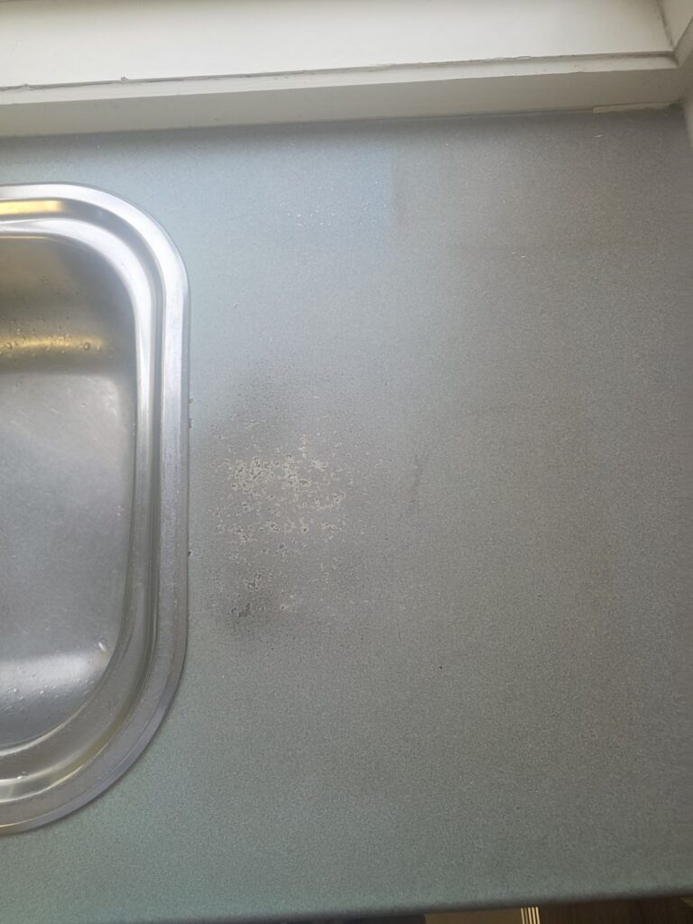 Close-up of worn, stained laminate benchtop beside sink before resurfacing, Hillside
