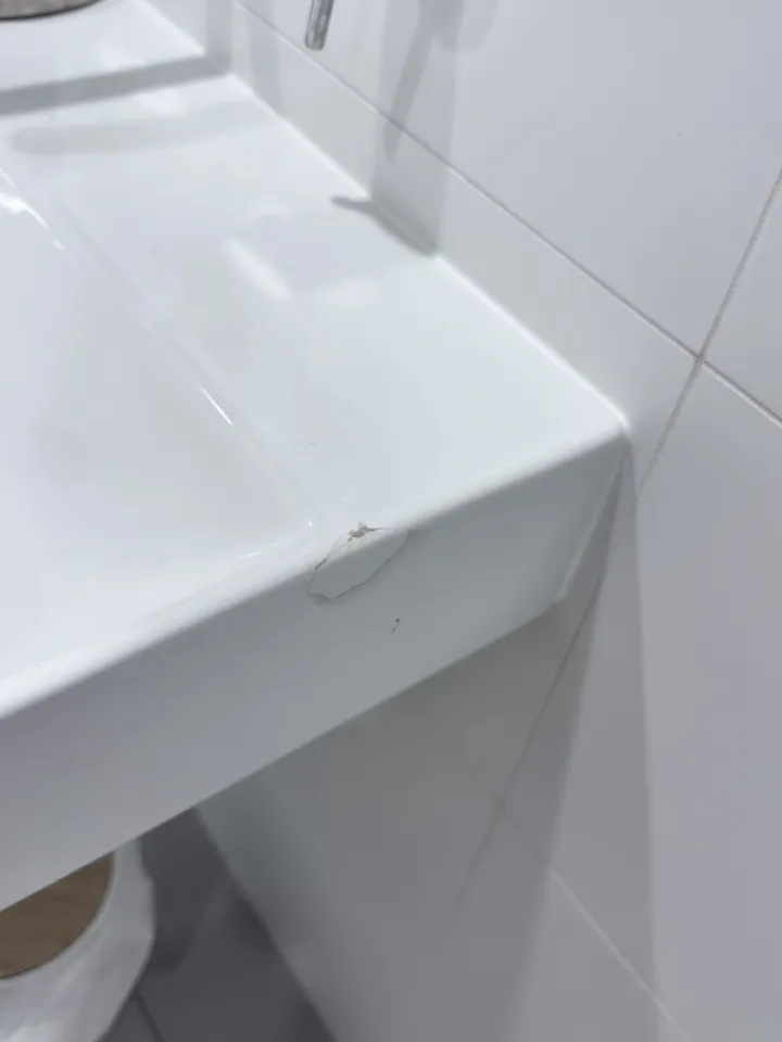 Corner of a white wall-hung basin with a chip in the front edge