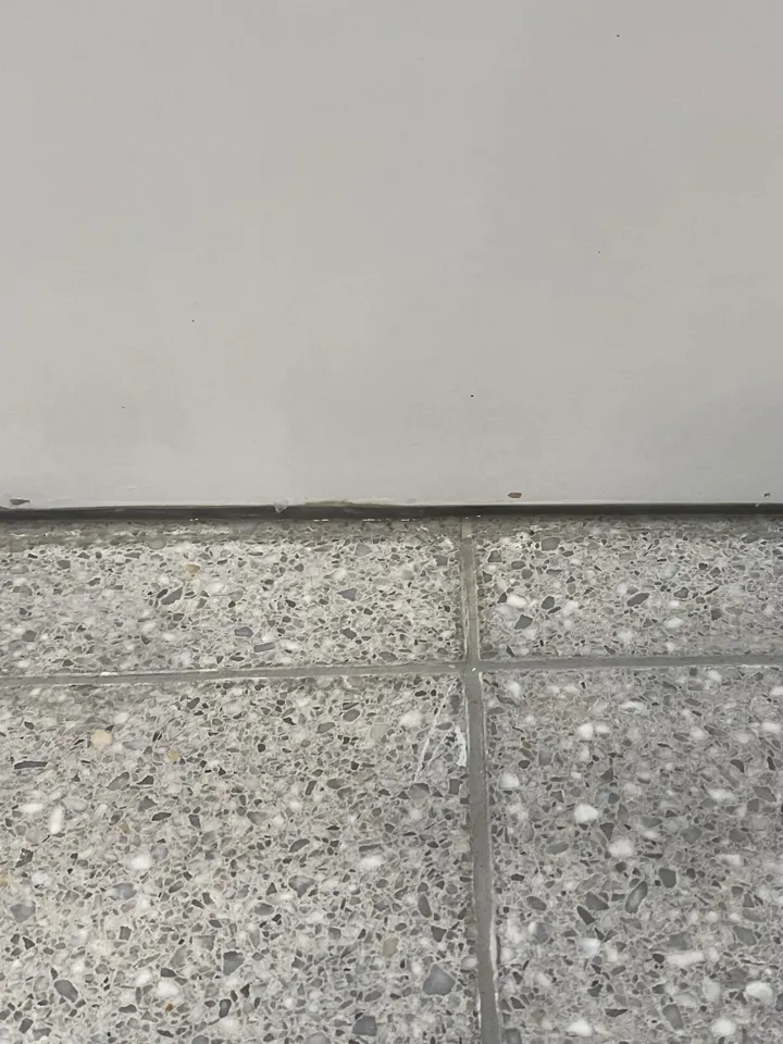 Bottom edge of a white freestanding bath on a terrazzo-look floor, with small chips along the edge