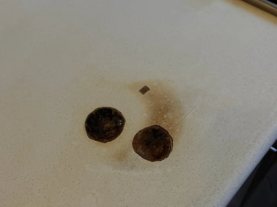 Pale speckled laminate benchtop beside a gas cooktop with two round black burns from hot pans