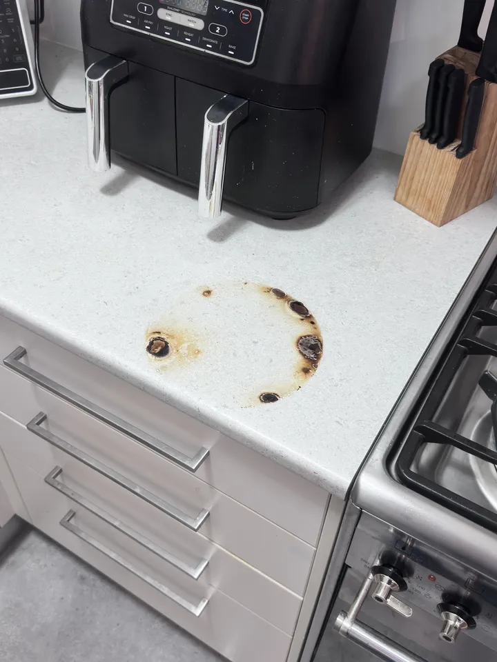 White stone-look laminate benchtop beside a gas cooktop with a round burn mark from a hot pan