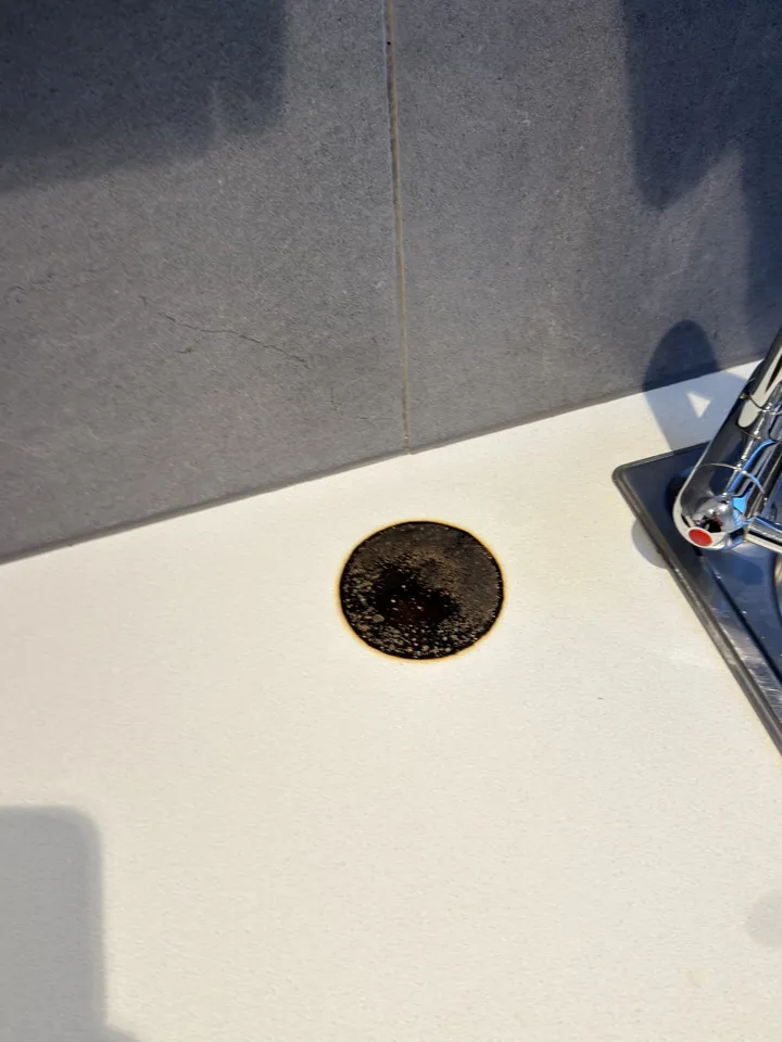 Cream laminate benchtop beside the sink tap with a large round black burn mark