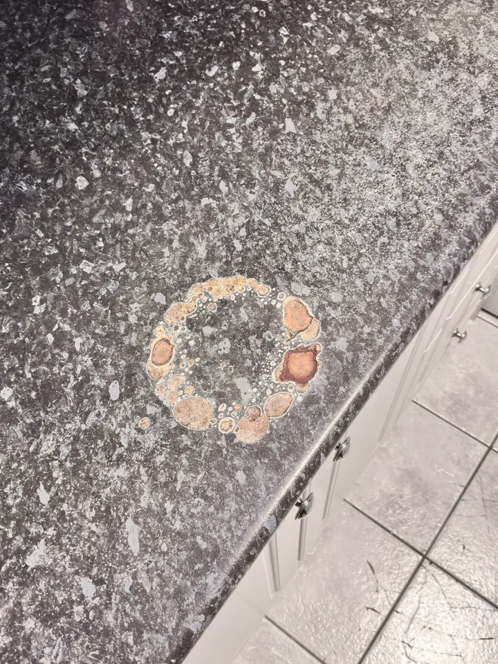 Dark granite-look laminate benchtop with a pale ring burnt into it by a hot pot