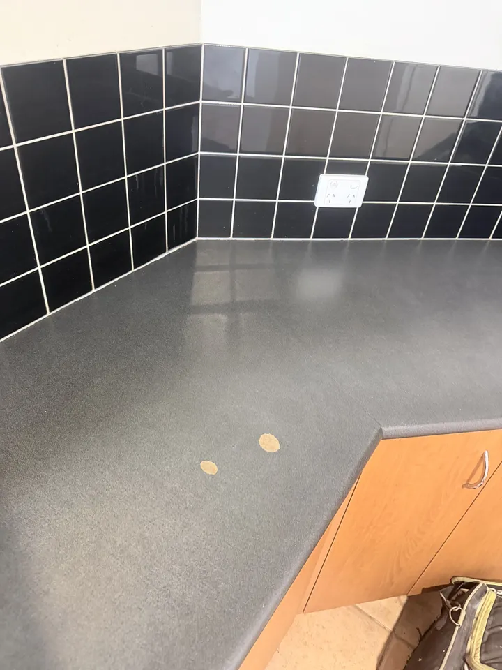 Dark stone-look laminate benchtop with two round chips showing the pale board underneath