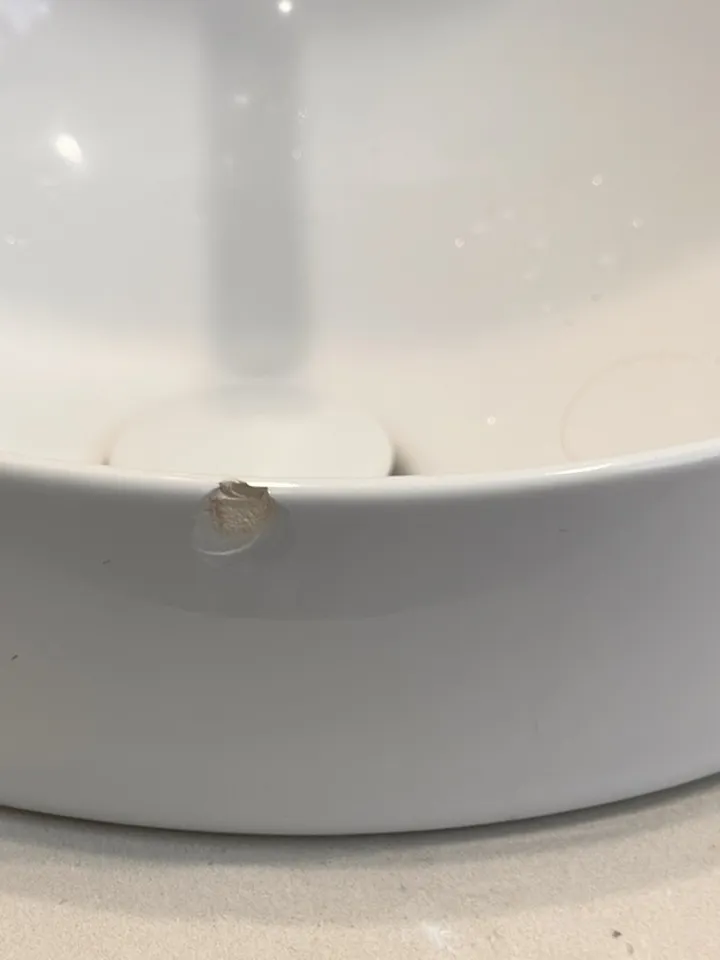 Inside of a round white vessel basin with a small chip on the front wall near the plug