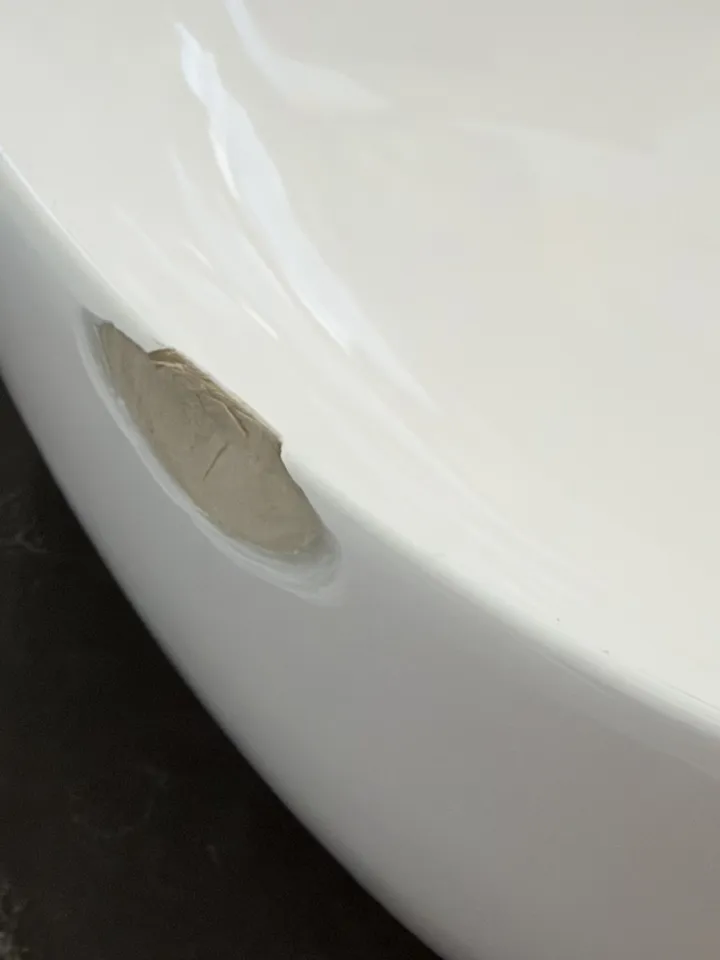Side of a white vessel basin on a dark stone top with a large chip showing the body underneath